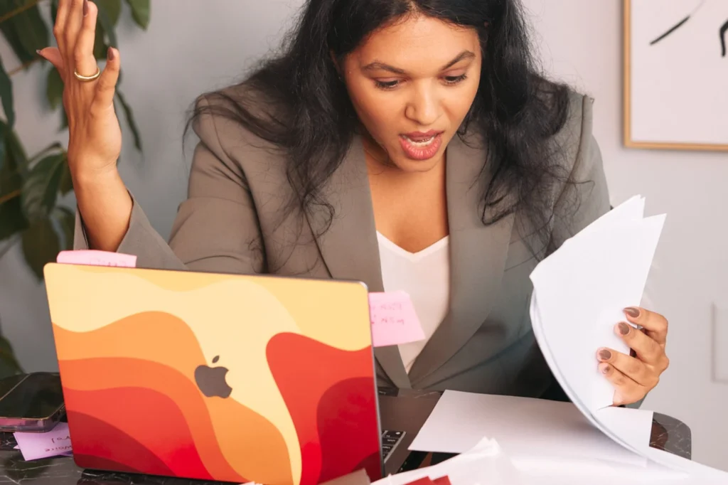 Woman (Nermin) looking at documents on her work desk. She looks surprised. In front of her is a laptop.