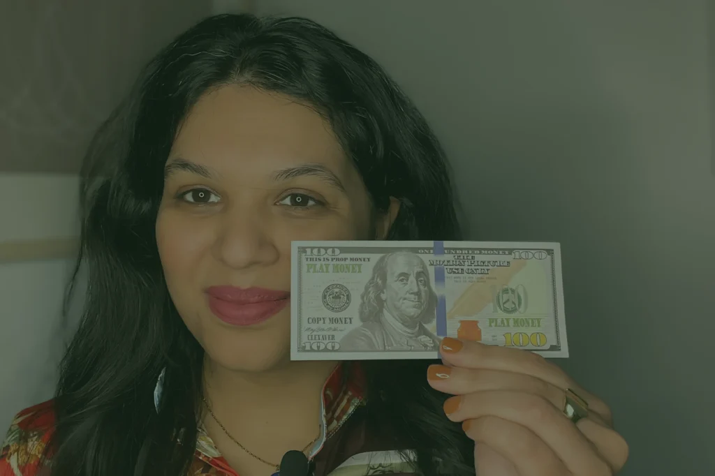 Woman (Nermin) holding a Dollar bill. She looks at the camera and smiles.