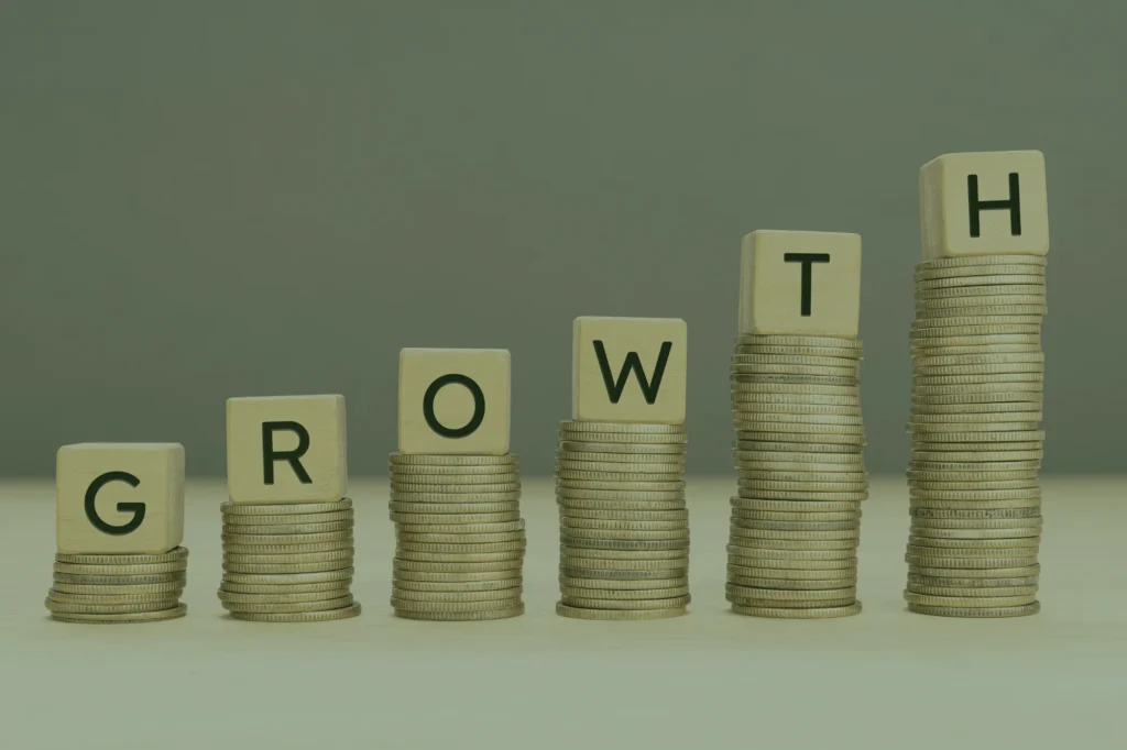Towers made of coins. Above each tower there is a wooden block with a letter on it. Together they form the word "Growth"